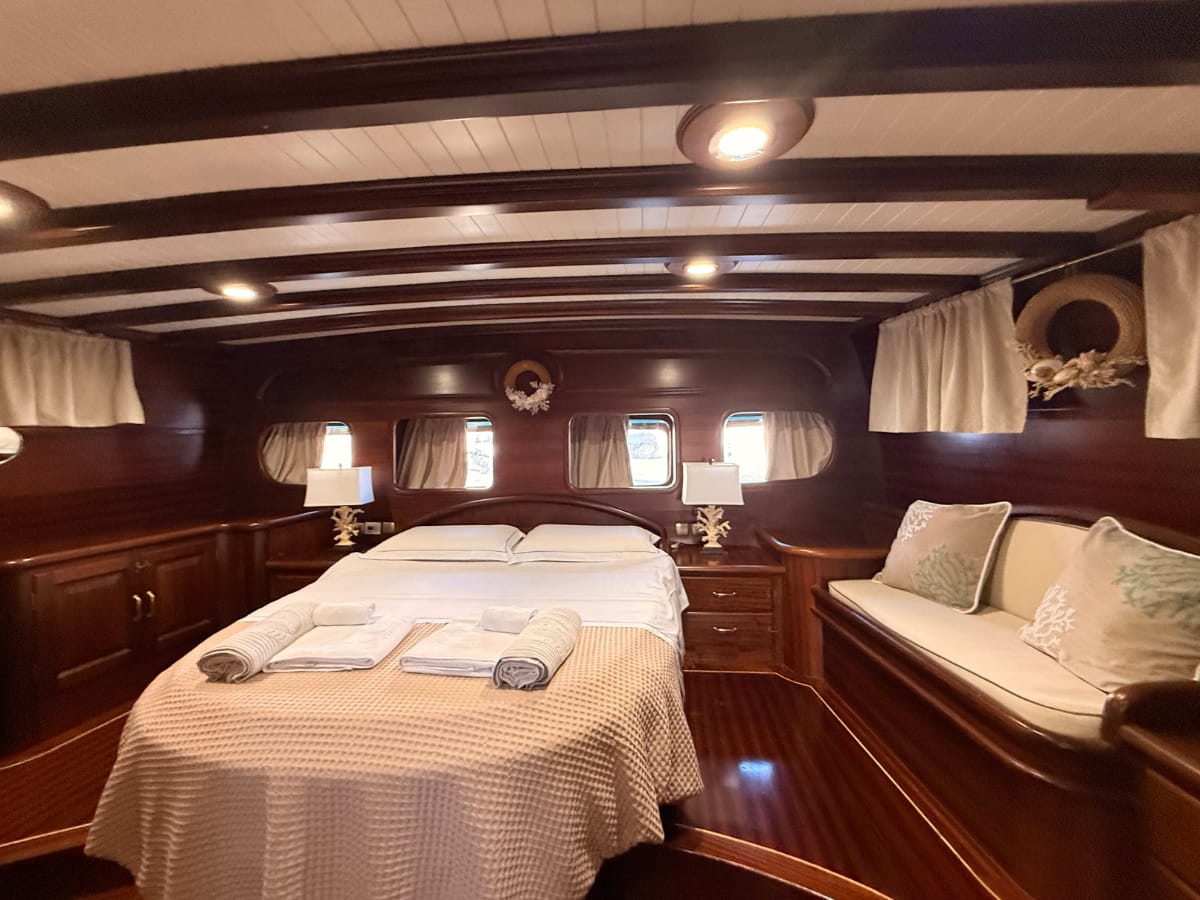 Ingresso cabina armatoriale. ampio letto con accesso laterale, divanetto con cuscini, grandi oblò di poppa, comodini e abat-jour in corallo, armadi e ghirlande di conchiglie
