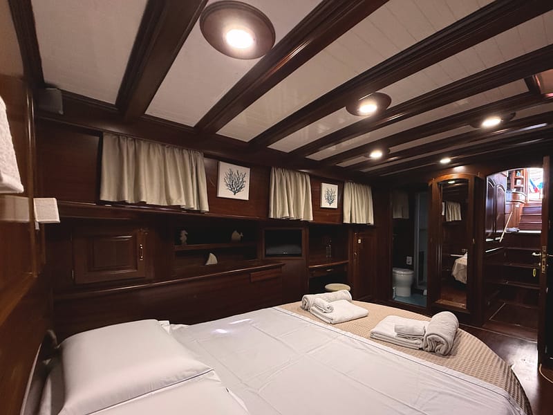 Cabina matrimoniale di prua. Vista del letto con tv in cameraoblò, asciugamani personalizzati, accesso bagno privato e specchio a tutta altezza
